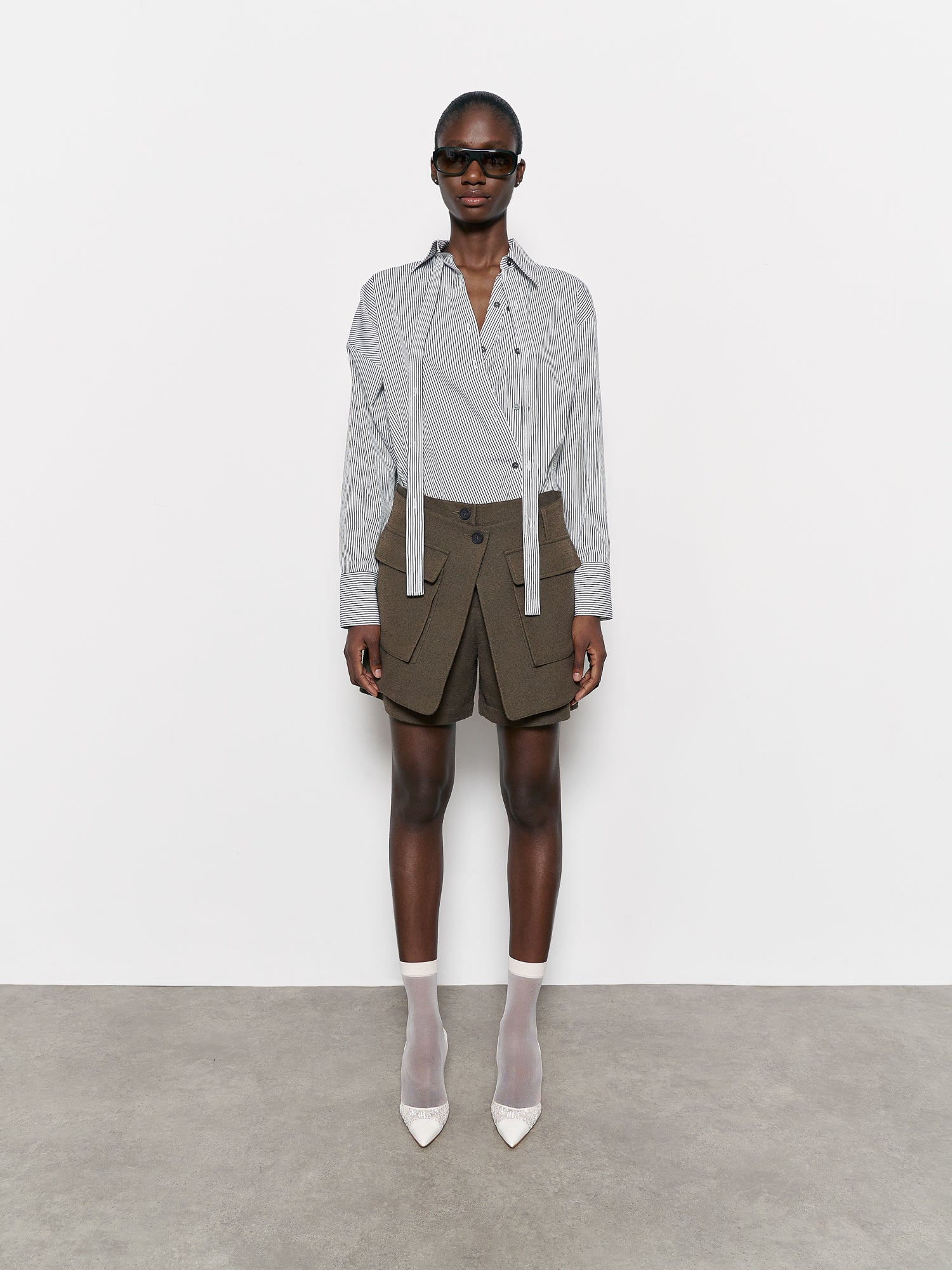 Model wearing a white and black stripe shirt , dark green shorts, and white shoes on a plain background